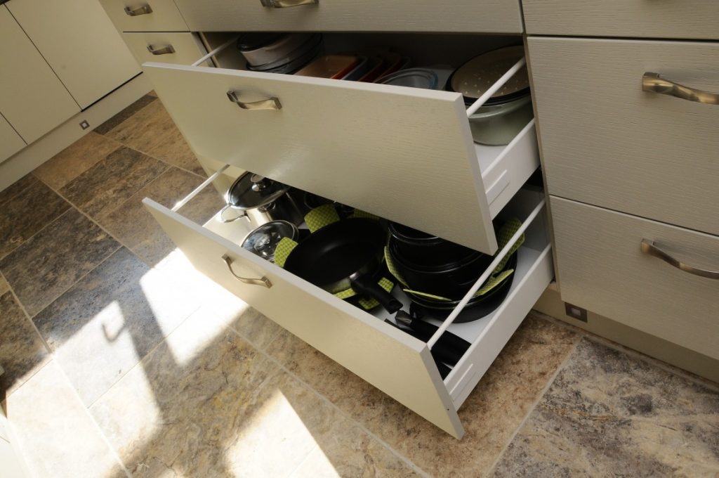 a set of white deep pan drawers slightly open so you can see the pans in the drawers and they also have green cloth pan protectors between the pans