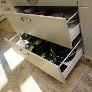 a set of white deep pan drawers slightly open so you can see the pans in the drawers and they also have green cloth pan protectors between the pans