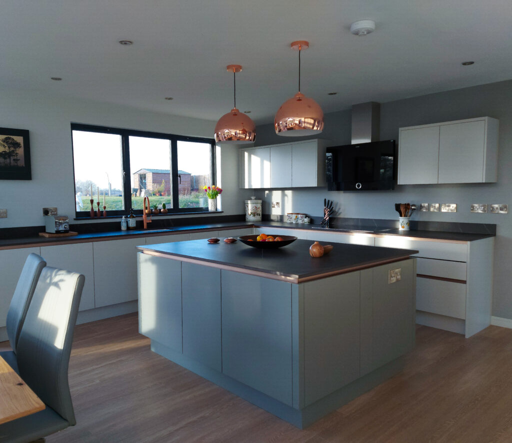 kitchen island in grey, has copper coloured pendant lights above it 